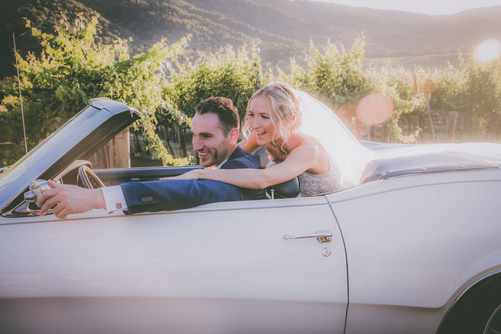 Groom and bride look into car mirror during sunset at a Carmel vineyard.
