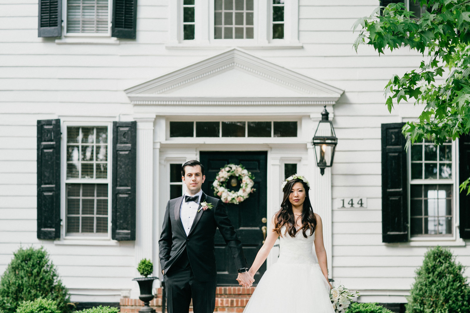 Groom and bride holding hands in front of the historic Fernbrook Inn House from the 18th century.