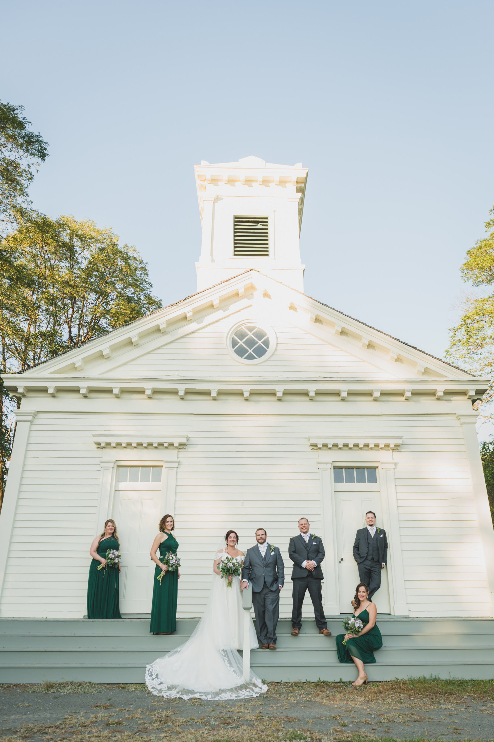 bride and groom with bridal party posing in front of white barn at The Barn at Old Bethpage