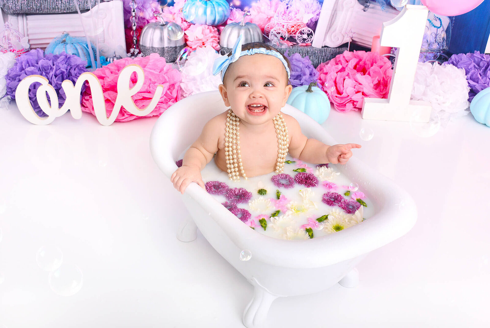 girl smiles while in a milk bath with purple flowers at a photostudio in houston