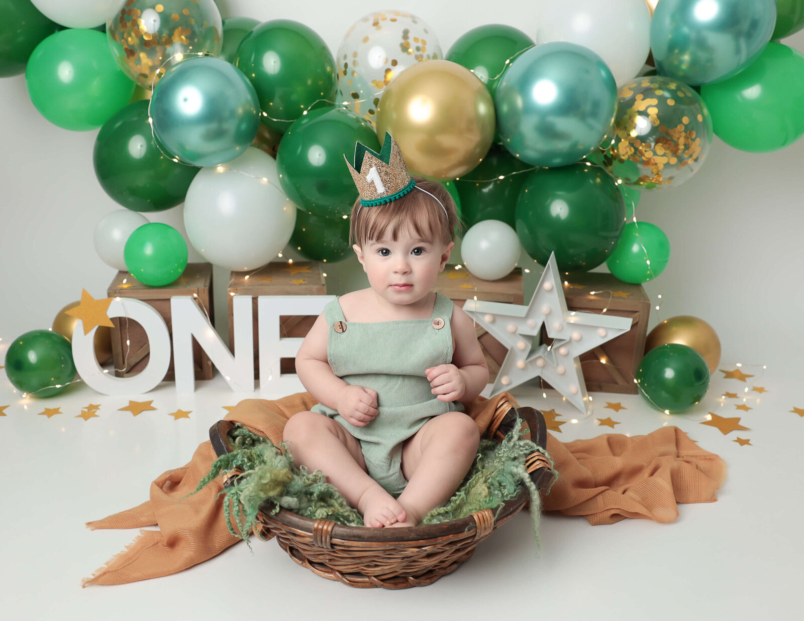 Cute boy in a basket with green balloons at our studio in Rochester, Ny.