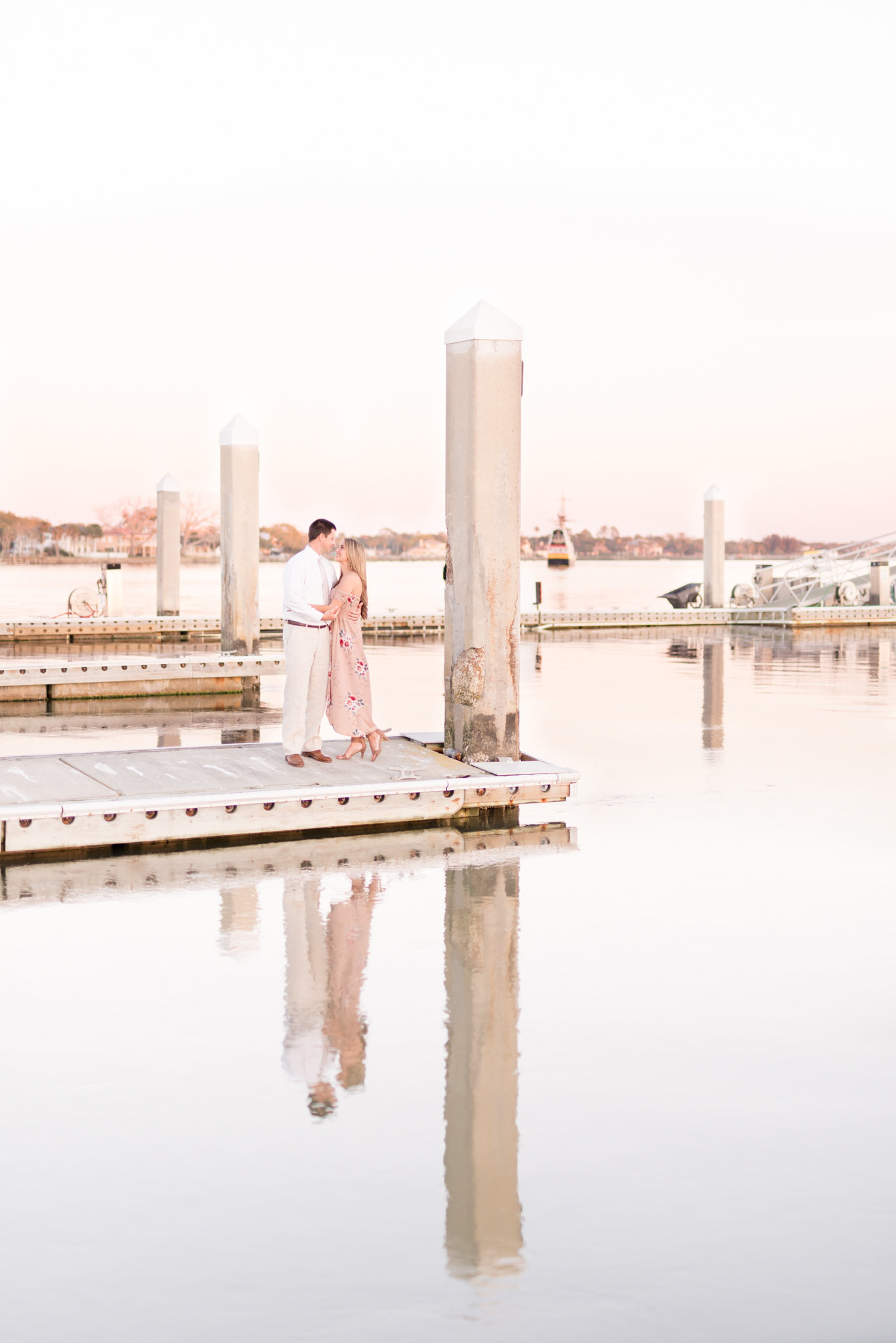 Man and woman stand on dock at sunset.