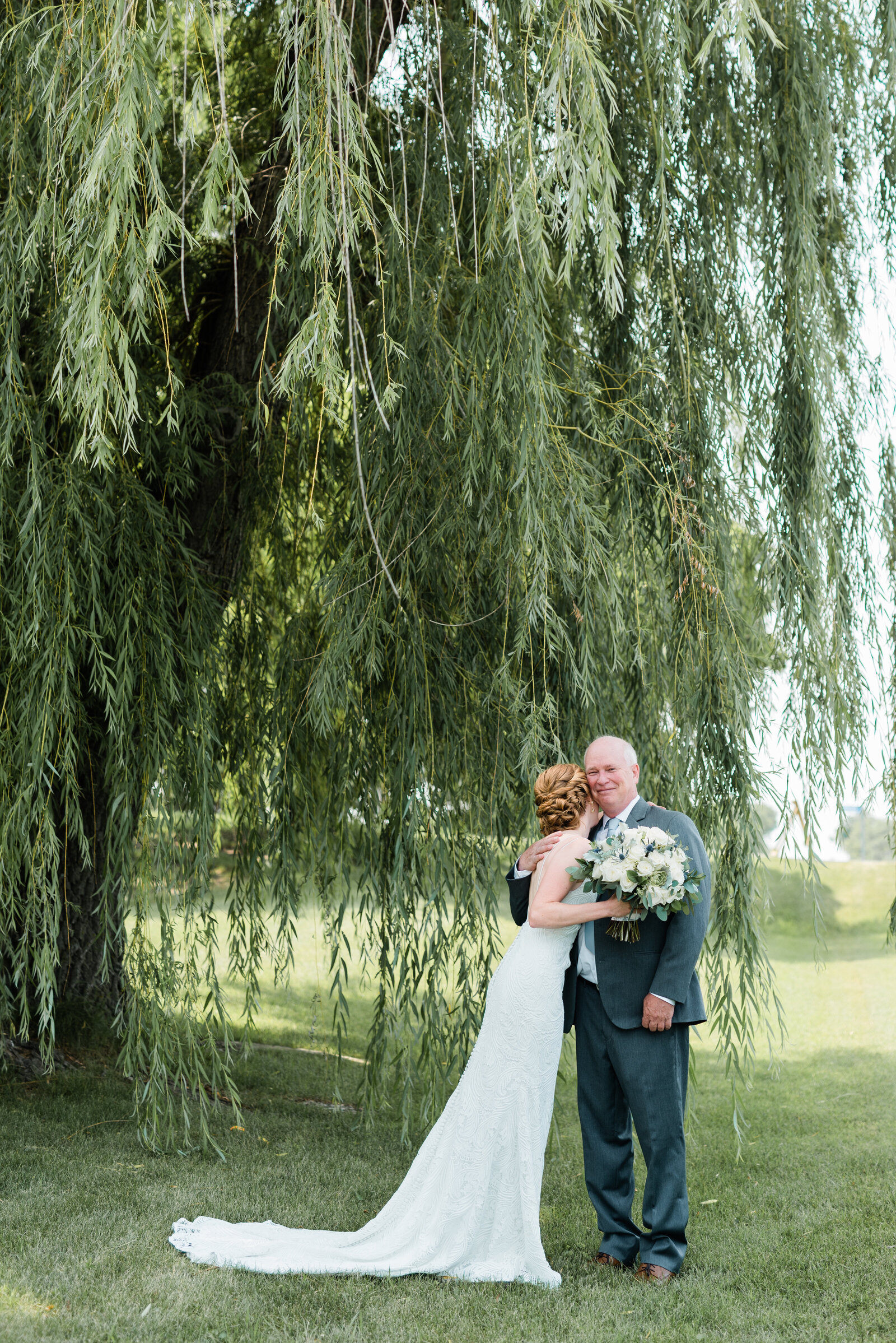 Bride and father of the bride hug below willow tree
