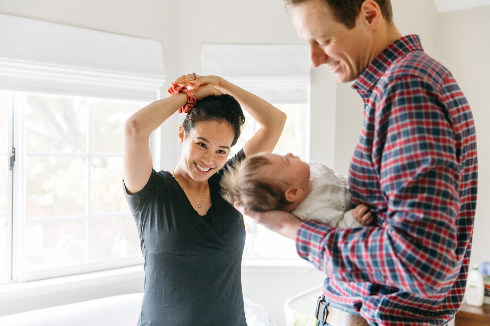 dad in plaid shirt holding newborn baby girl while mom looks on and ties up her hair