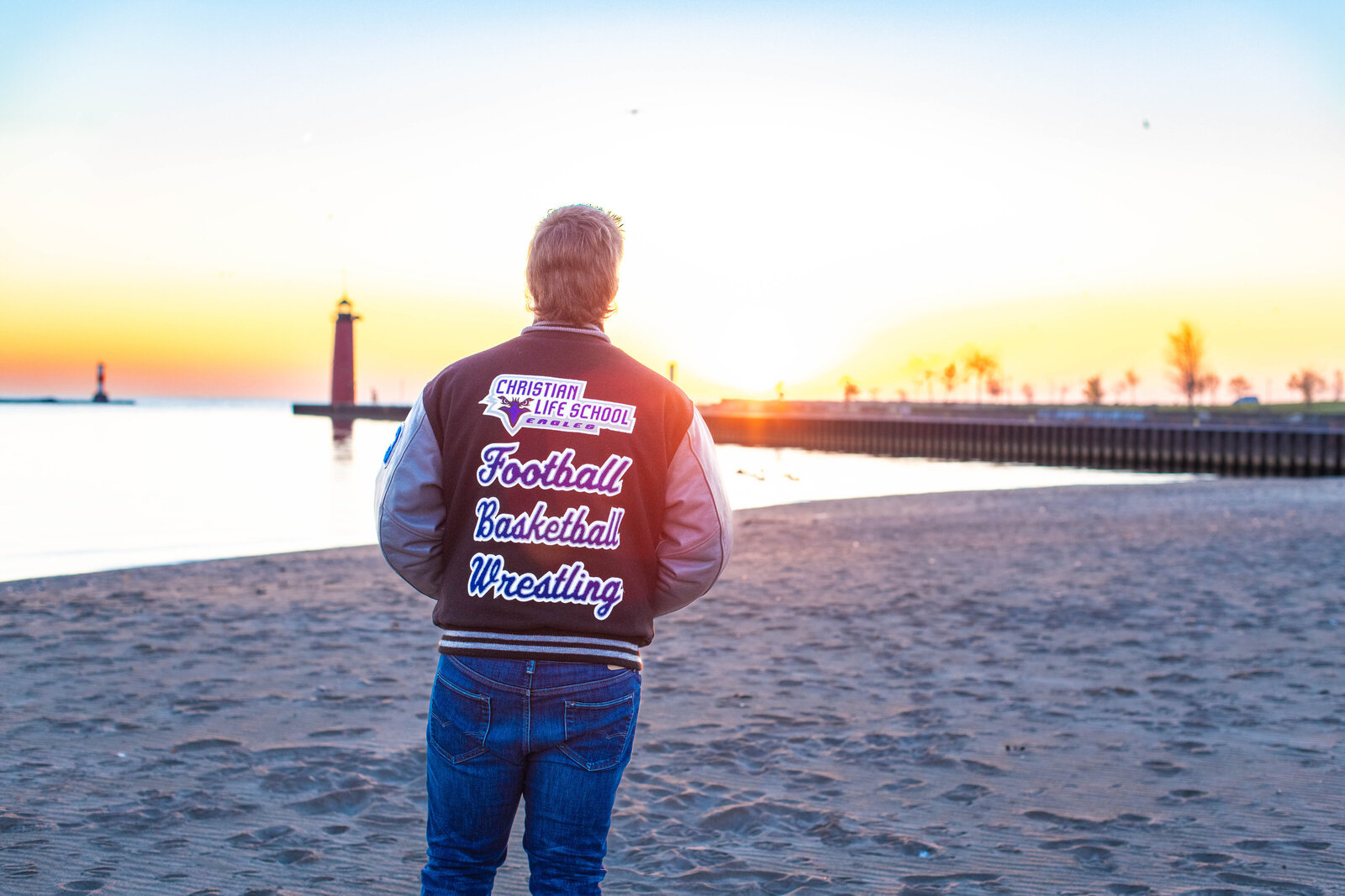 senior boy on beach and lake in lettermans jacket