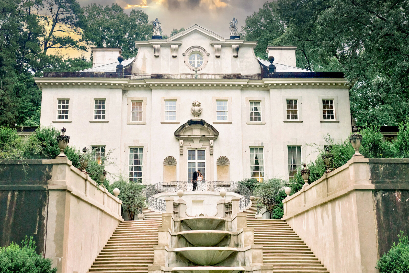 Editorial Swan House Portrait with Dramatic Clouds Editorial wide shot of bride and groom kissing in front of Swan House with dramatic cloudy sky in Atlanta