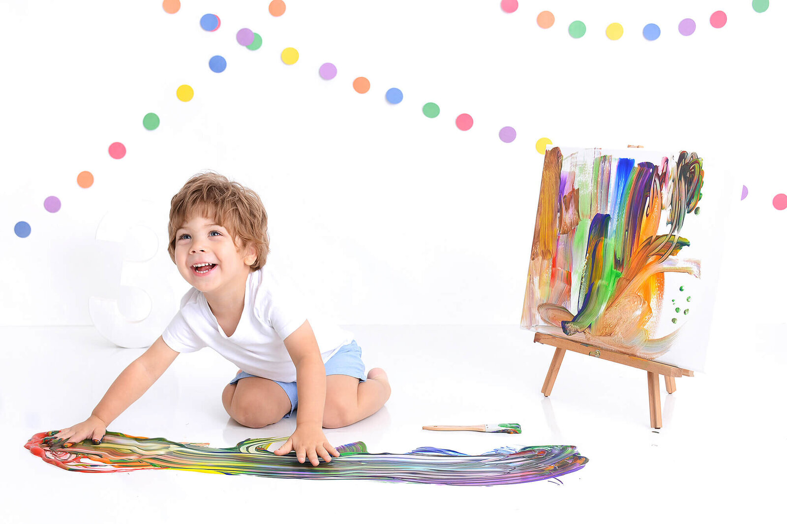 boy smiles and has fun playing with paint at his birthday photoshoot