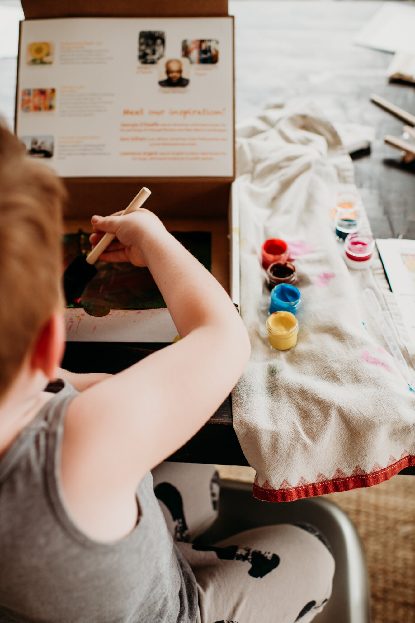 Branding Photographer, a young boy holds a sponge paint brush with paints beside him on the table