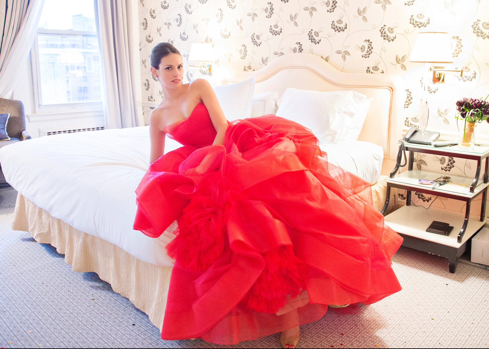 Woman in a red ballgown reclining on bed