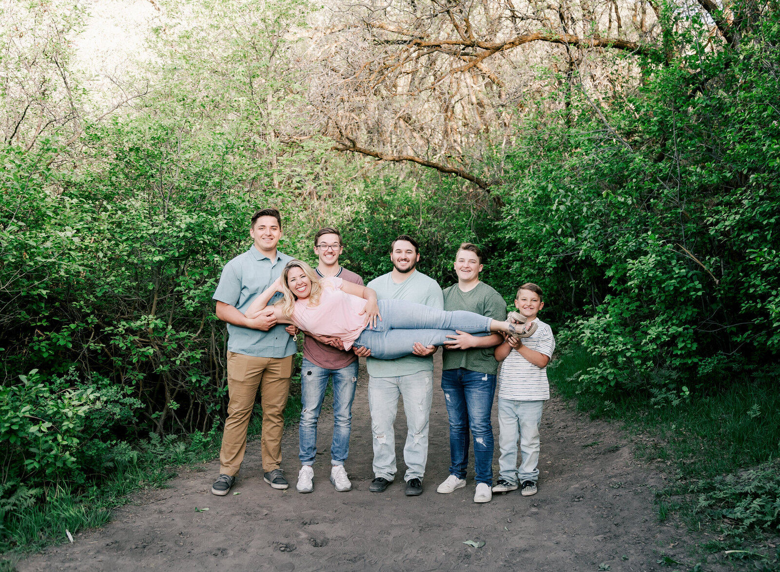 A family of boys holds up their mother in a fun pose during an outdoor family session.