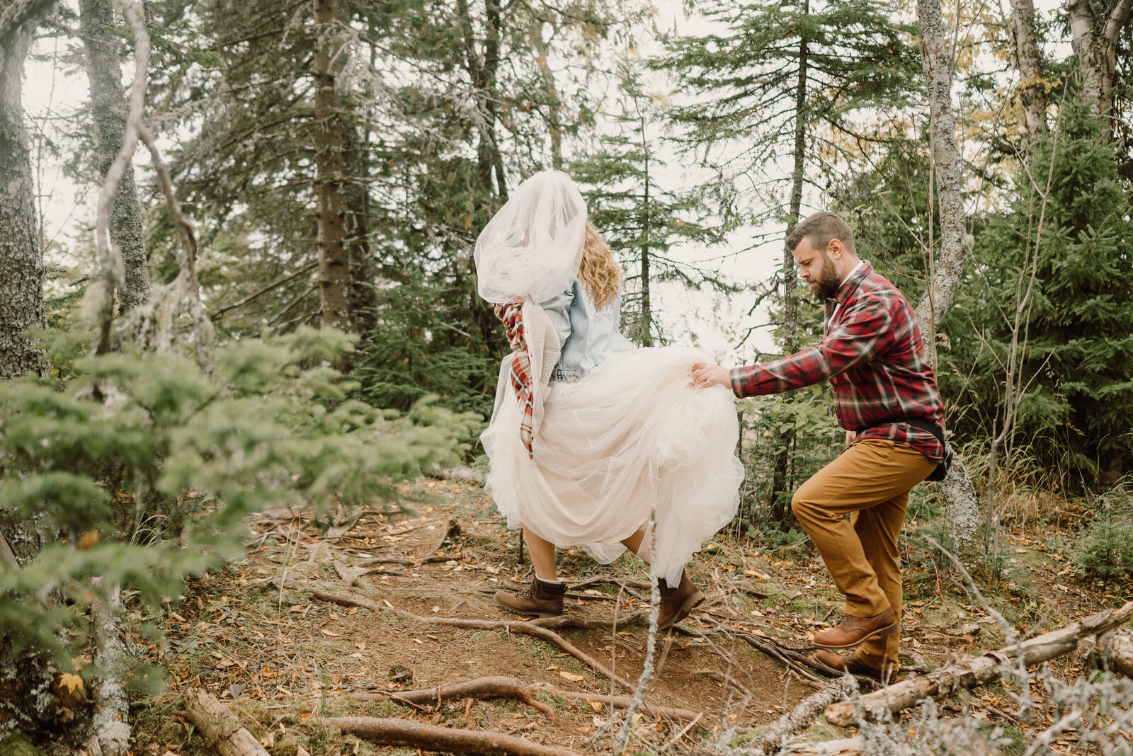Groom help bride carry her dress and hike through forest