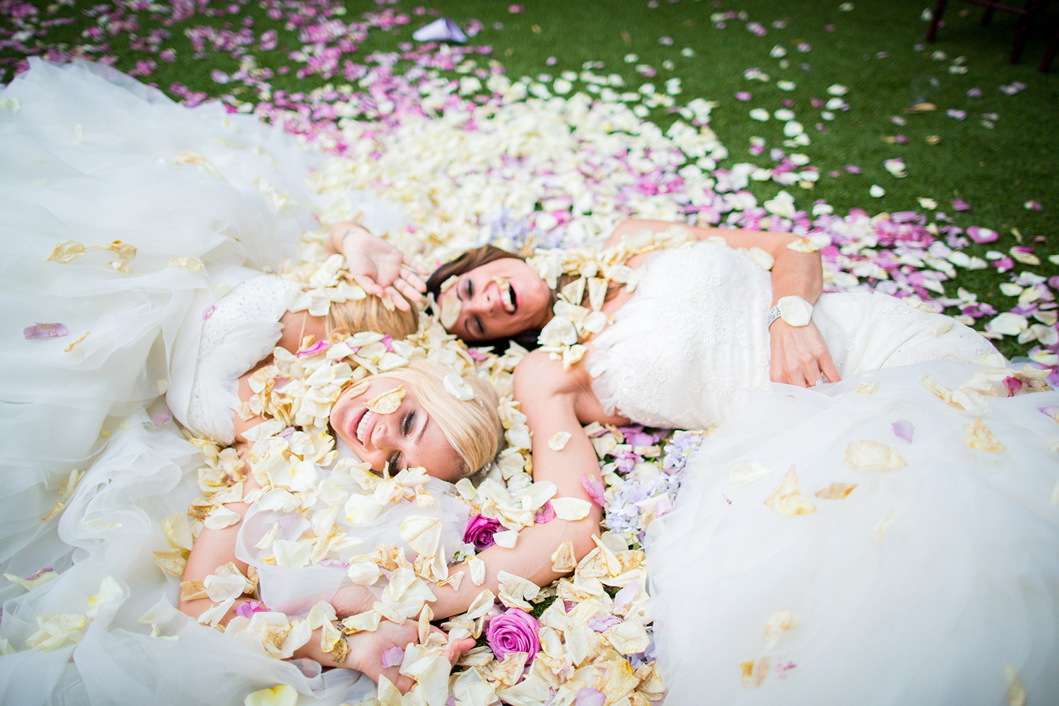Lesbian brides laying on a bed of flower petals at their wedding