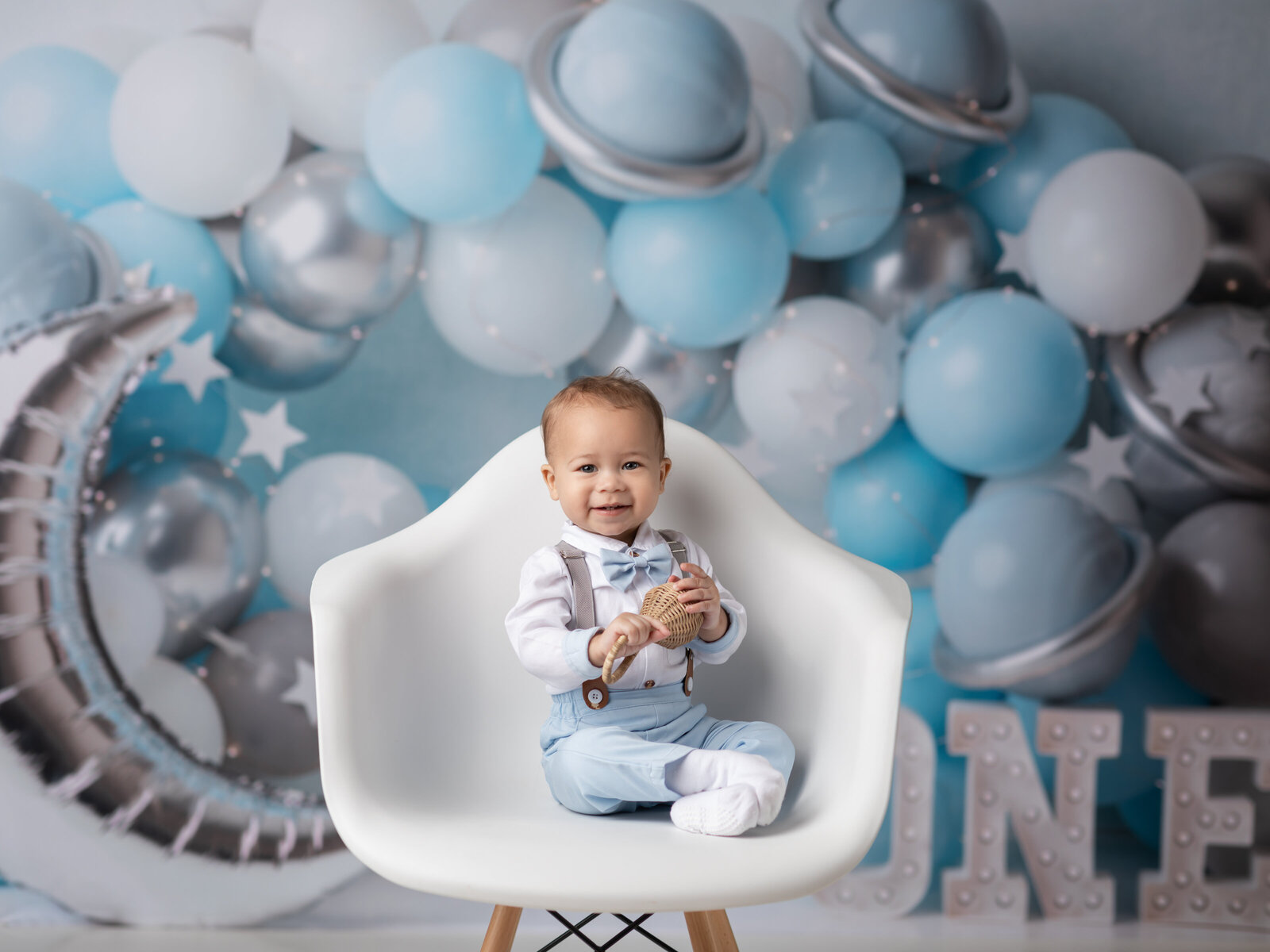 one year old boy sitting in white chair for cake smash photoshoot