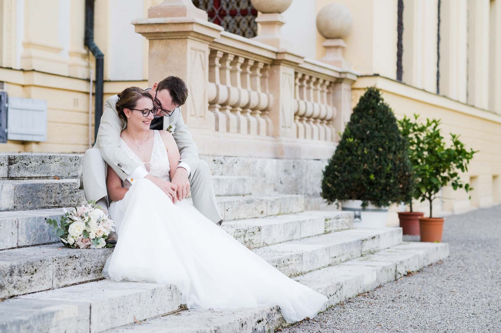 Ein Brautpaar sitzt auf stufen in park von Schloss Lustheim und Schloss Schleißheim nach Hochzeit