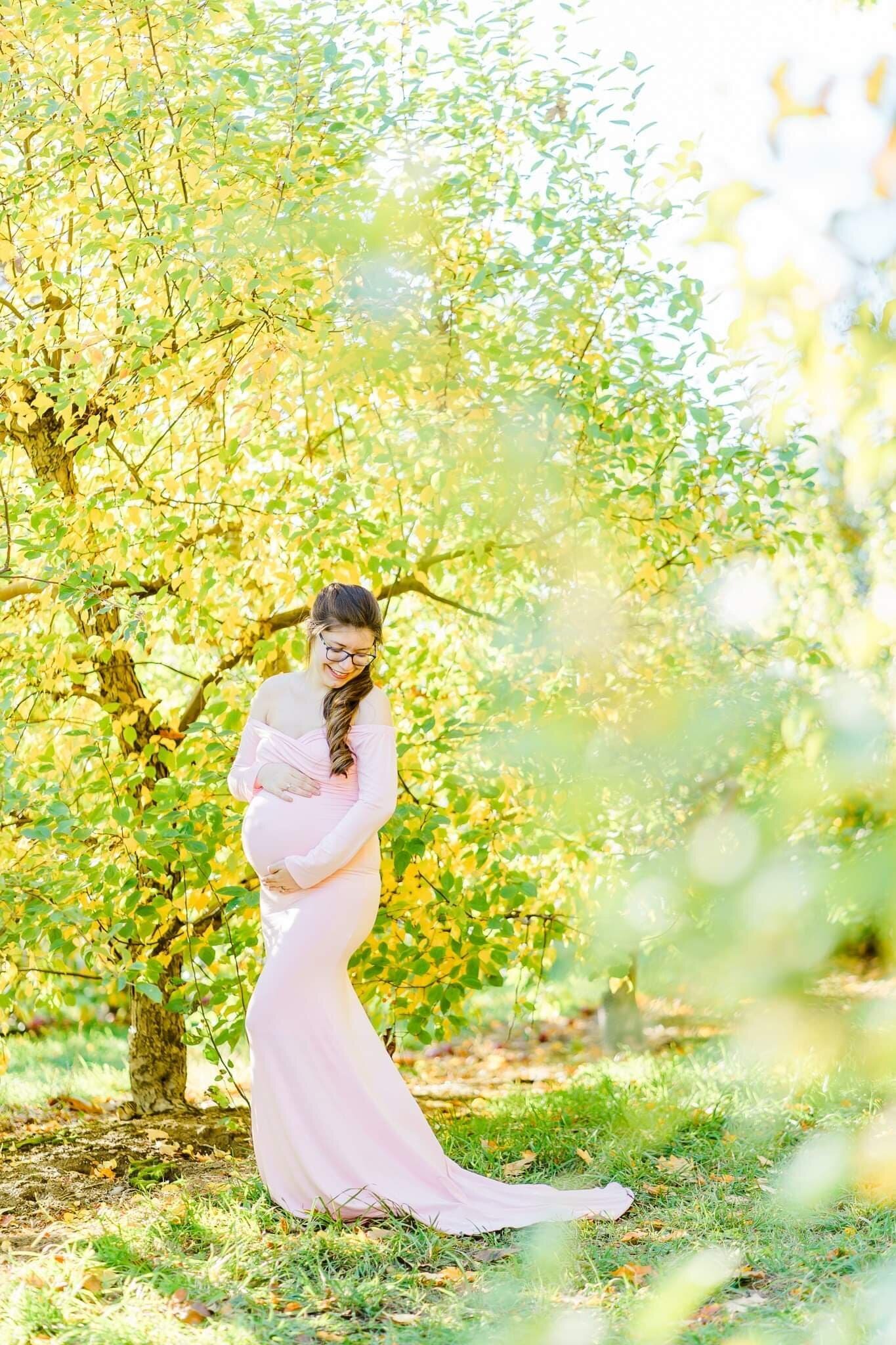 New Hampshire woman in pink dress holding belly for pregnancy photos