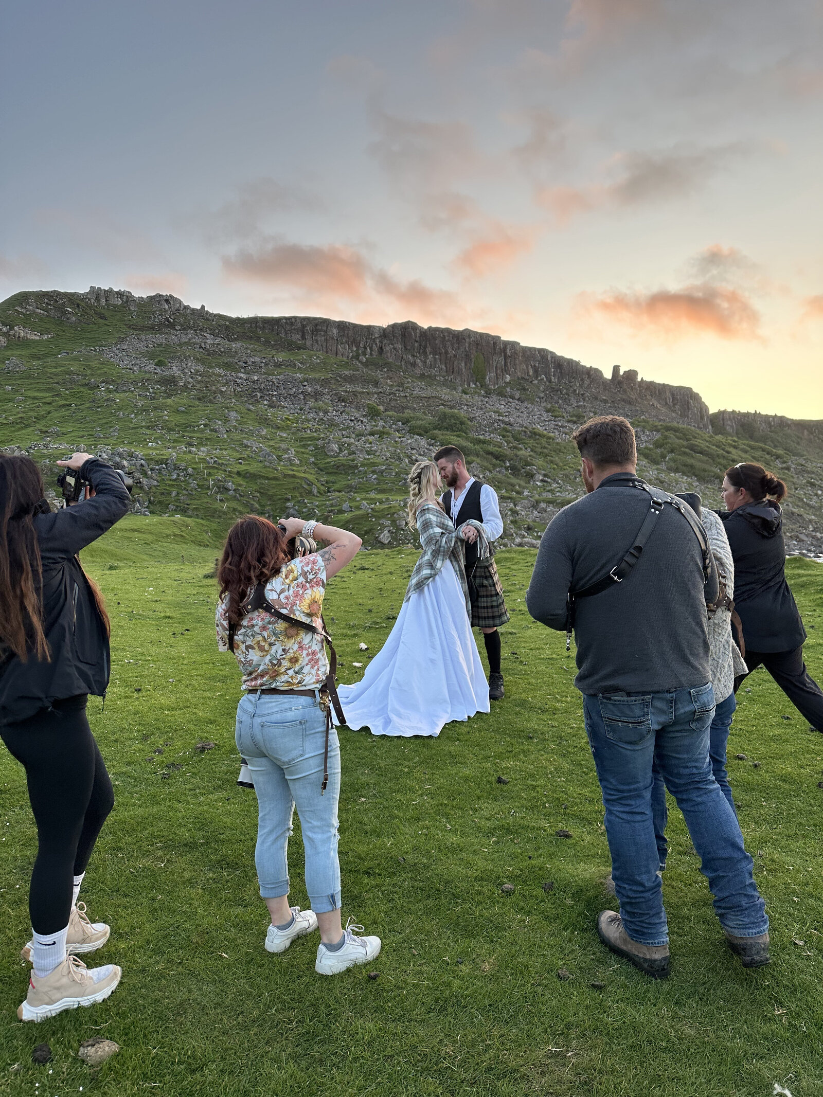 A joyful bride and groom in wedding attire celebrate on rocky cliffs by the sea at sunset, channeling the spirit of an Oregon coast photography retreat for wild-hearted artists.