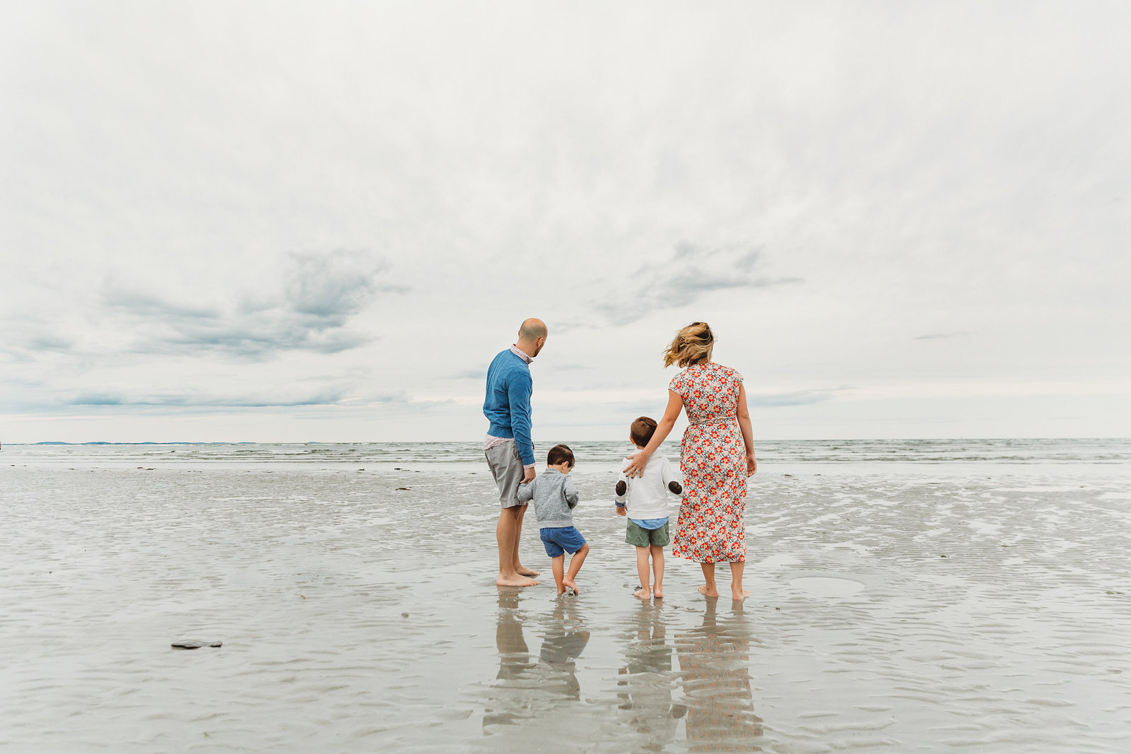 family with two boys stands and stares at ocean during family photo session in boston