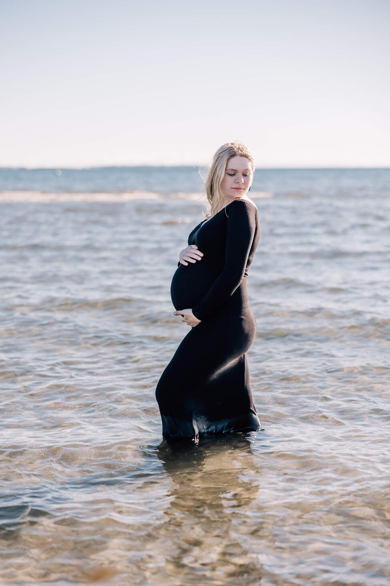 Pregnant woman in black dress in shallow water looking over her shoulder