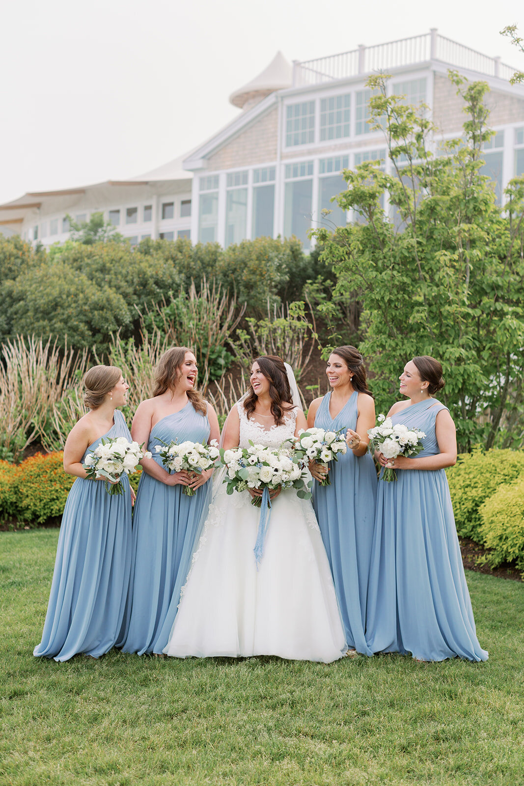 A bride and her bridesmaids smiling and holding bouquets of flowers.