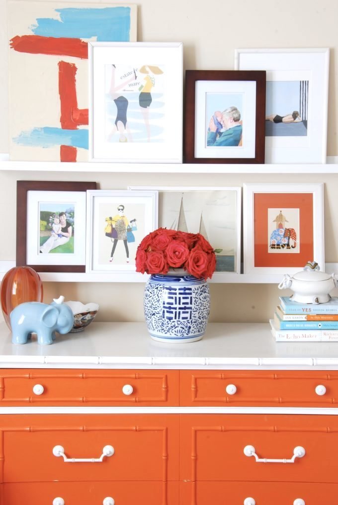 An orange white dresser with accessories and framed art and photos on shelves.