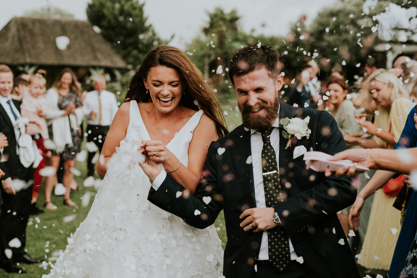 Bride and groom running and laughing as guests throw confetti