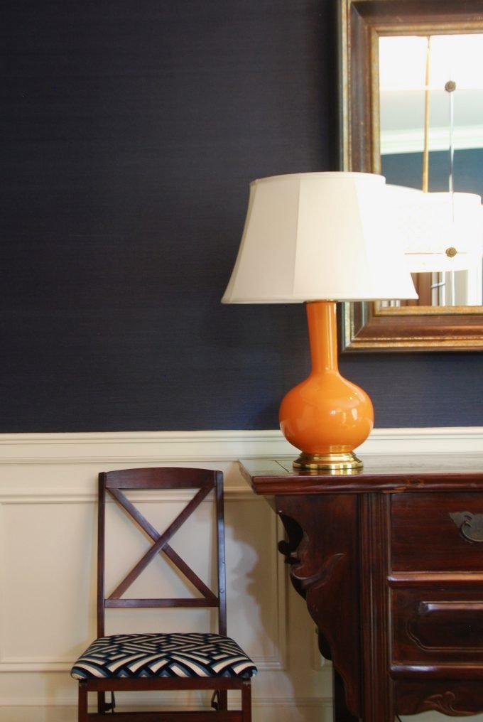 An orange lamp on a wooden sideboard next to a chair.