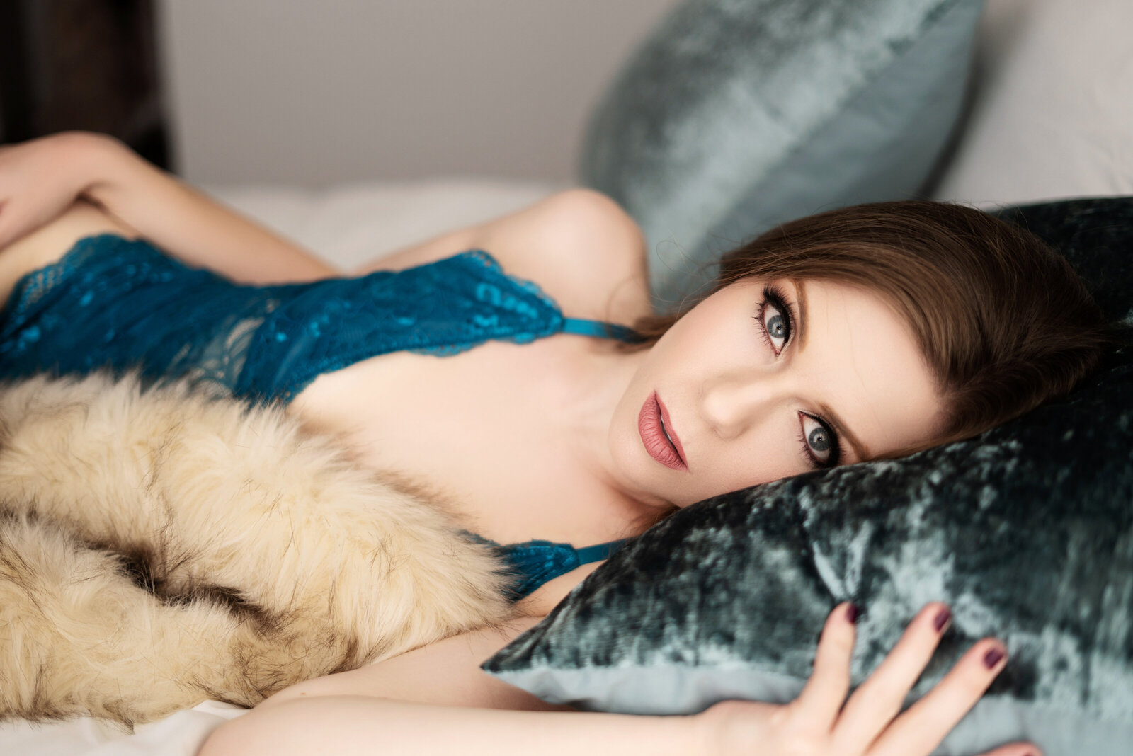 blue eyed woman laying on bed looking at the camera in teal lingerie