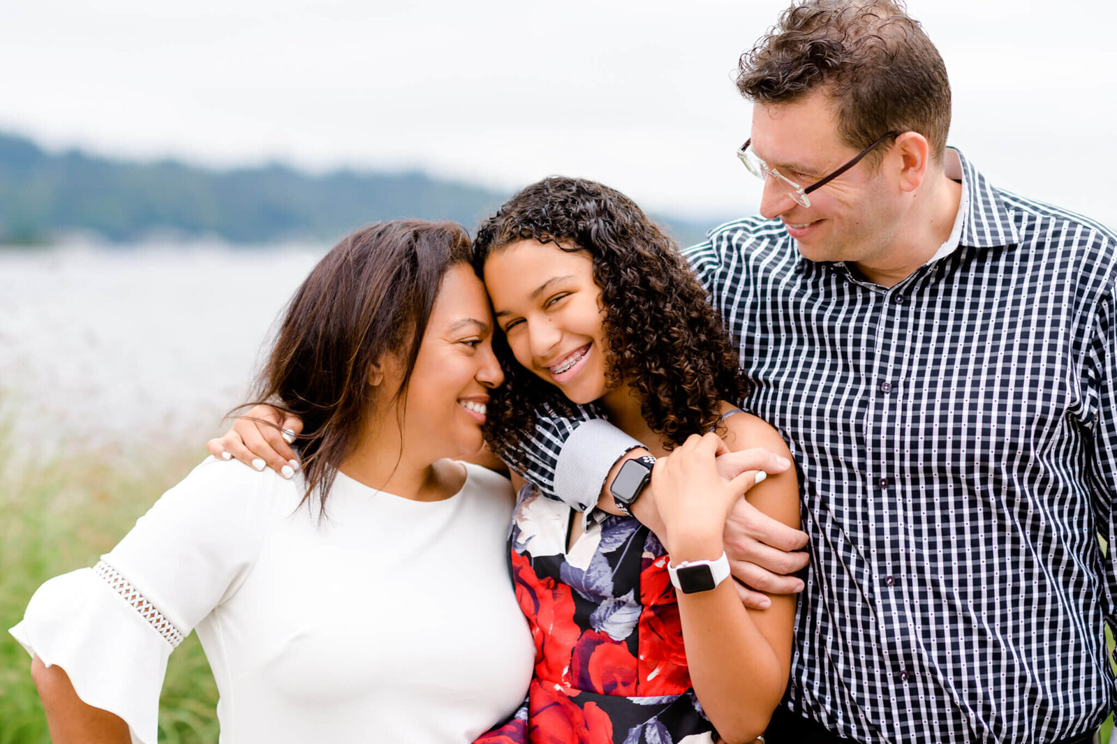 Happy mom and dad hug their teen daughter in a lakeside park