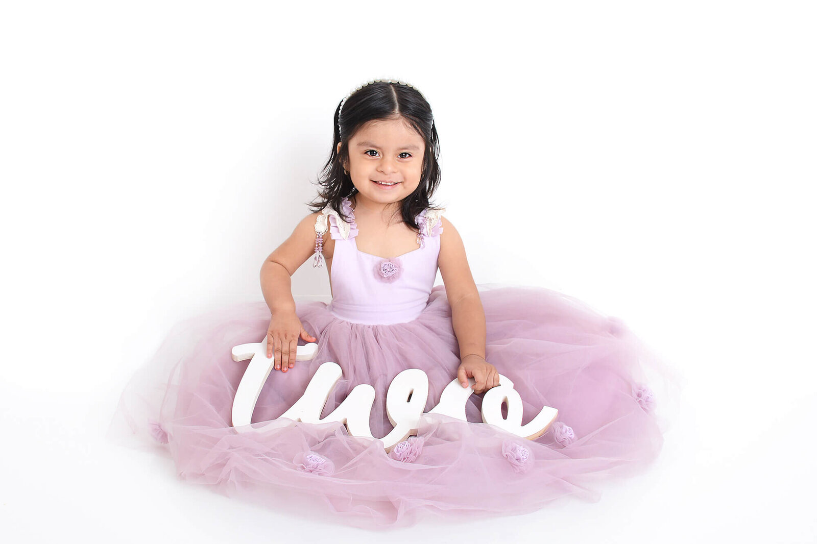 girl smiles while in a purple dollcake dress holding a two sign at her simple photoshoot