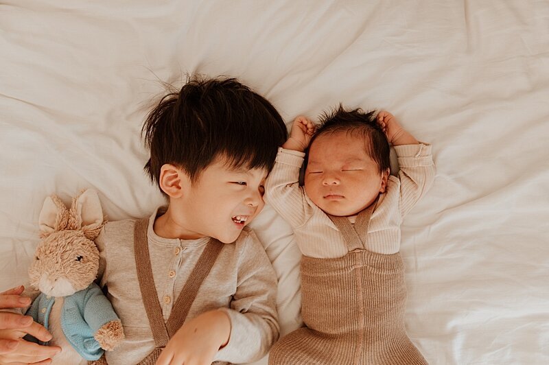 Photo of big brother laying on bed with baby brother by Vancouver newborn photographer