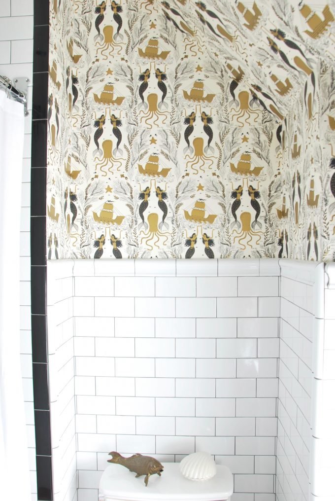 A wallpapered bathroom with subway tile.