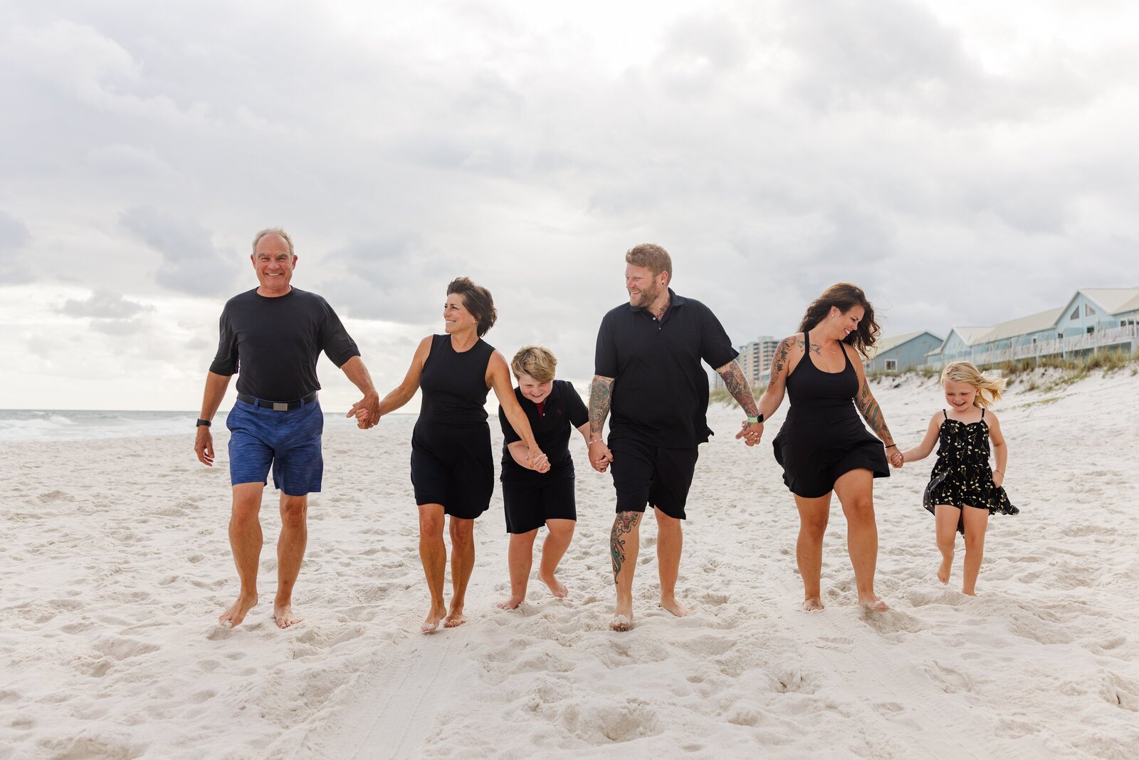Family holding hands and walking down beach during extended family beach session on Pensacola Beach