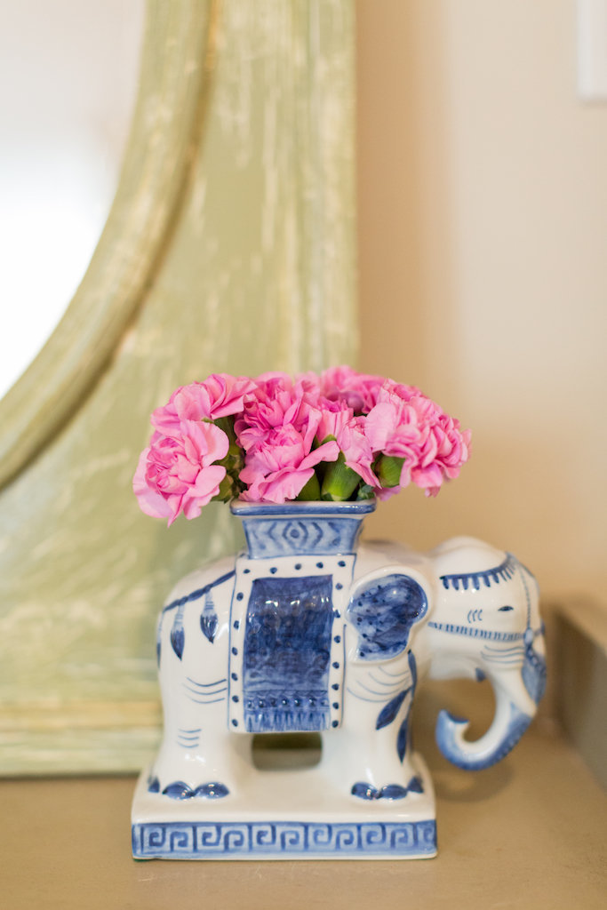 A white and blue ceramic elephant vase with pink flowers.