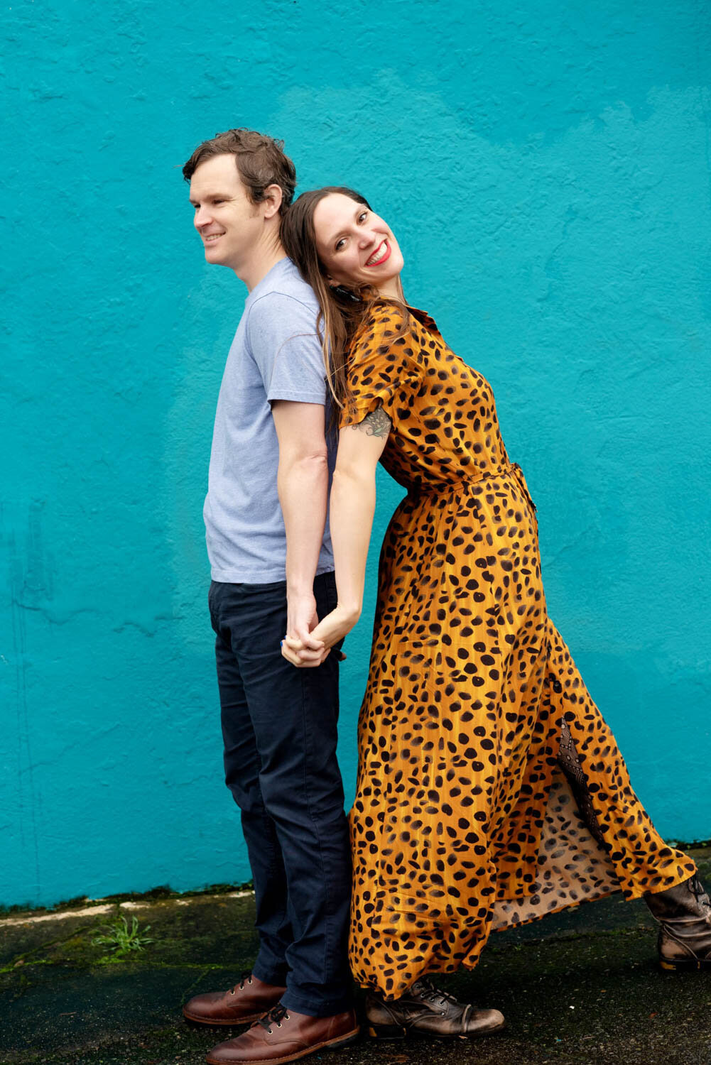 a woman in a leopard dress leans against a man in front of a bright blue wall