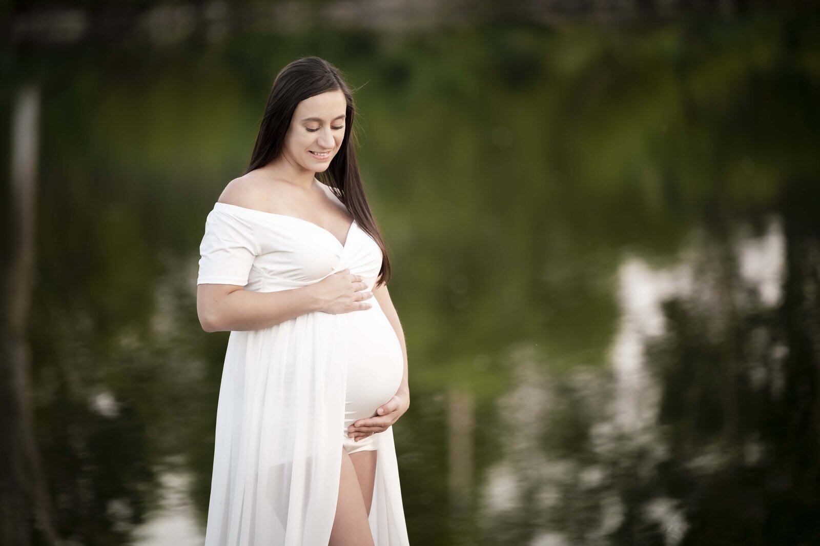 Pregnant woman holding belly with water behind her in Elkhart Indiana area