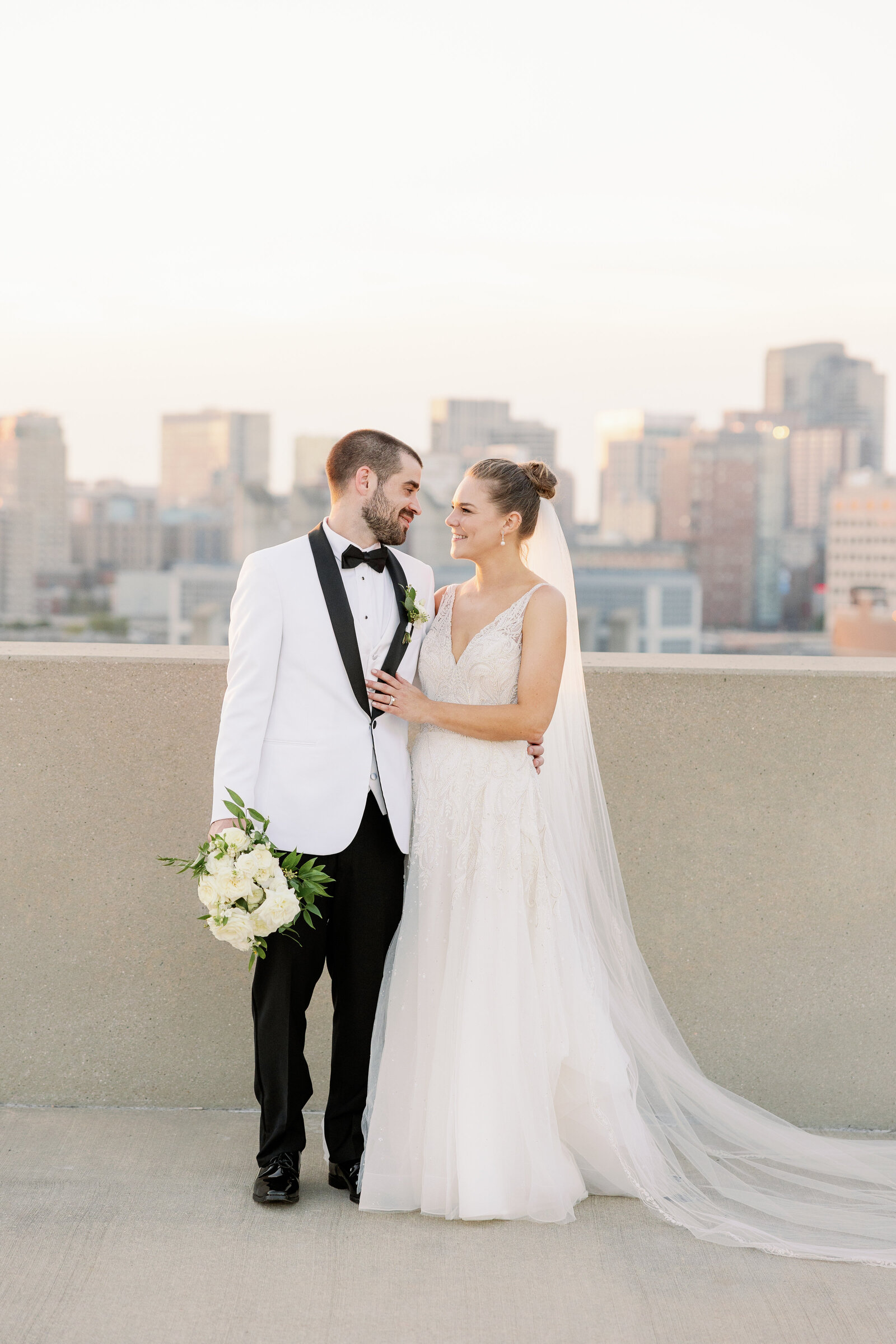 Wedding couple standing on a rooftop overlooking a city skyline.