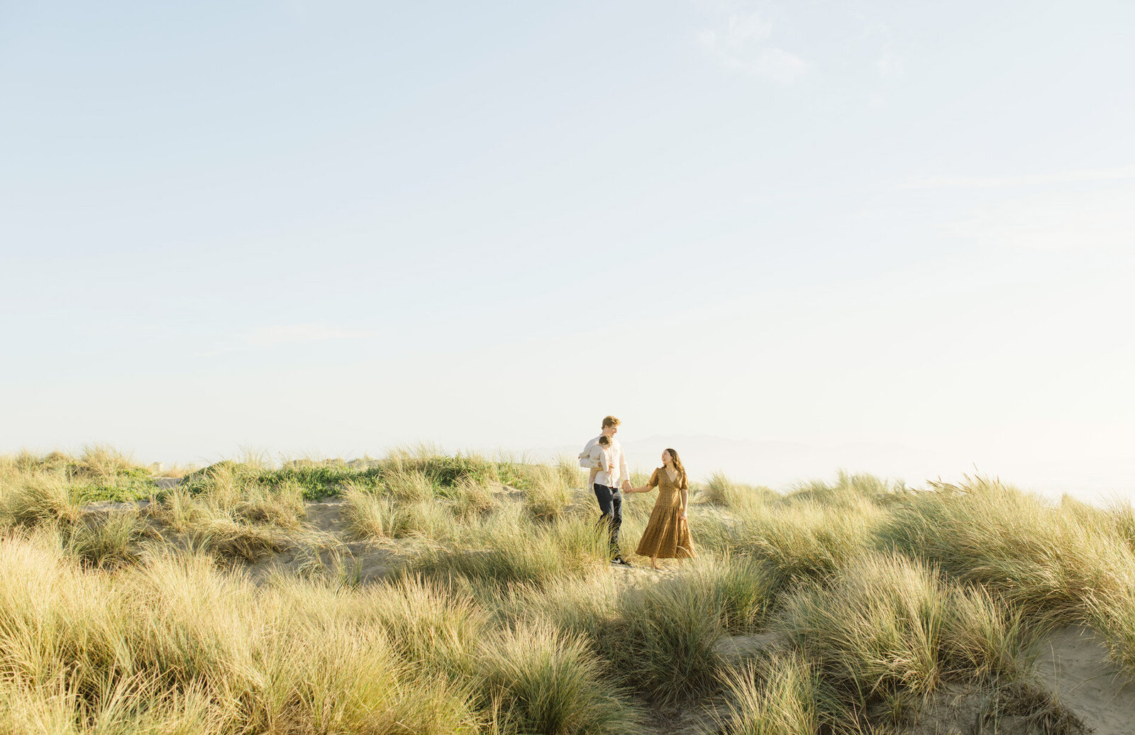A couple walks through tall grass, holding their baby, captured by Tevi Hardy, SF and Bay area photographer.
