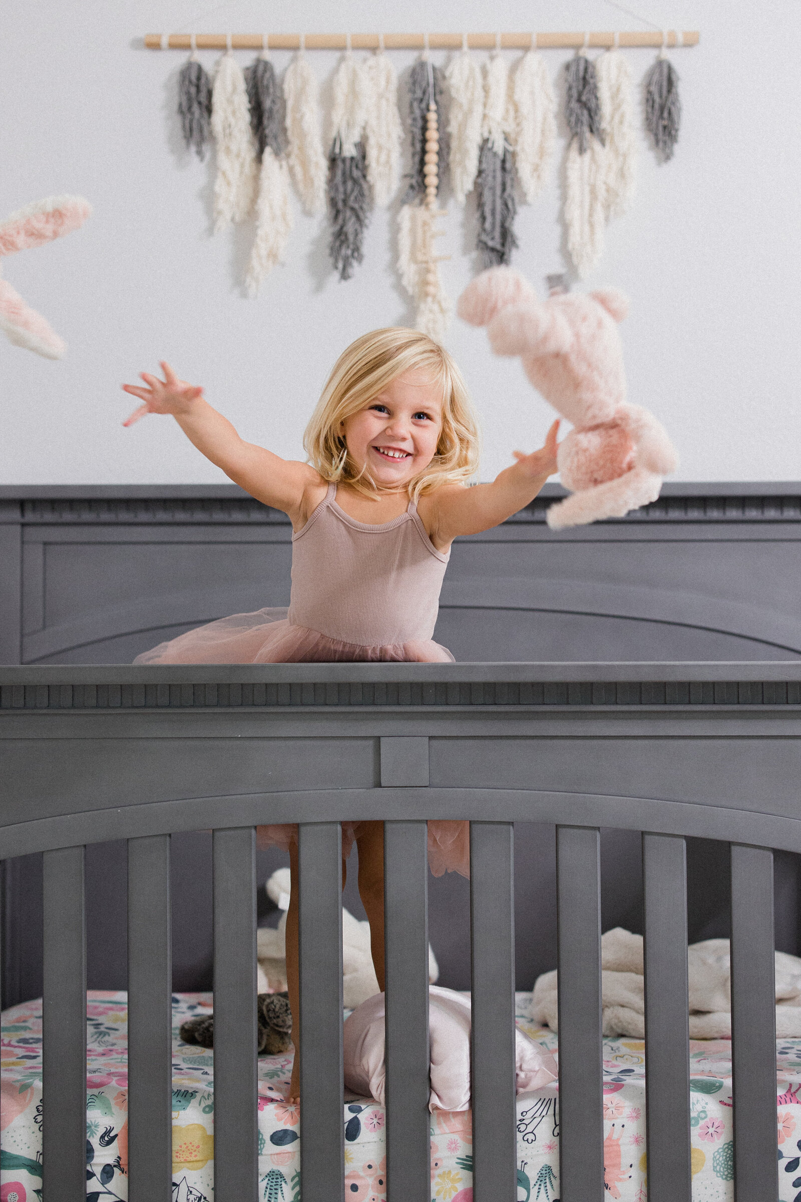 A little girl throws her stuffed animals out of her crib while laughing
