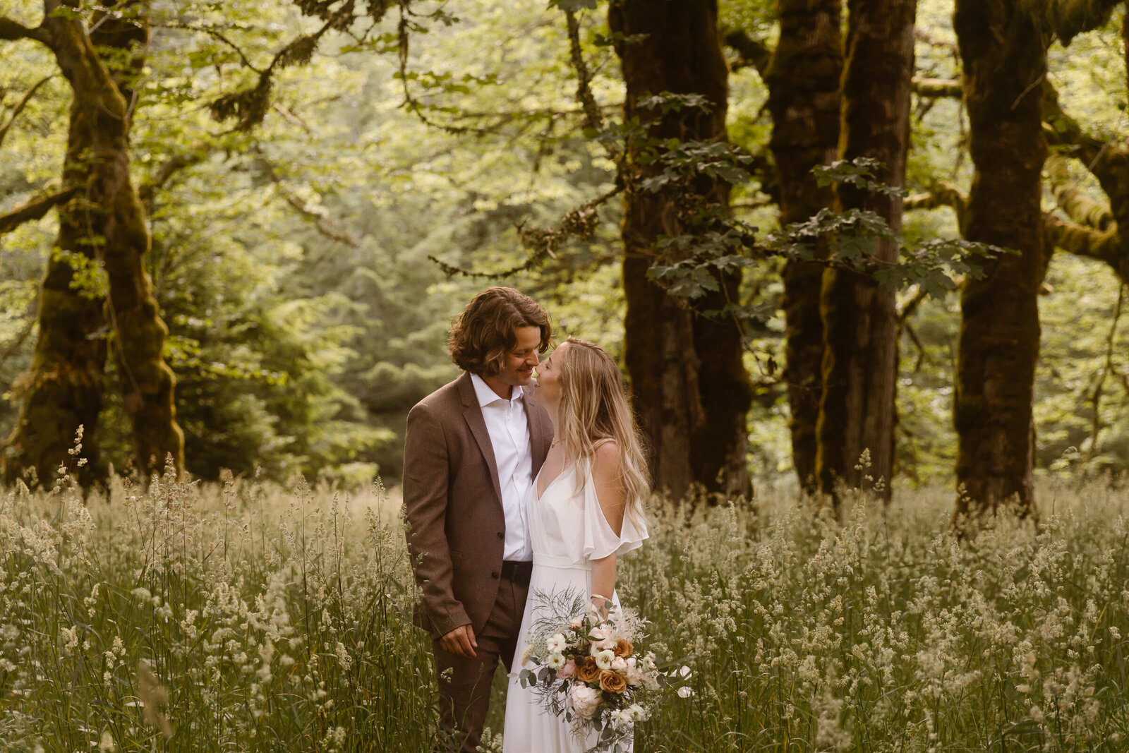a couple in wedding attire kisses in a field surrounded by trees at Washington elopement