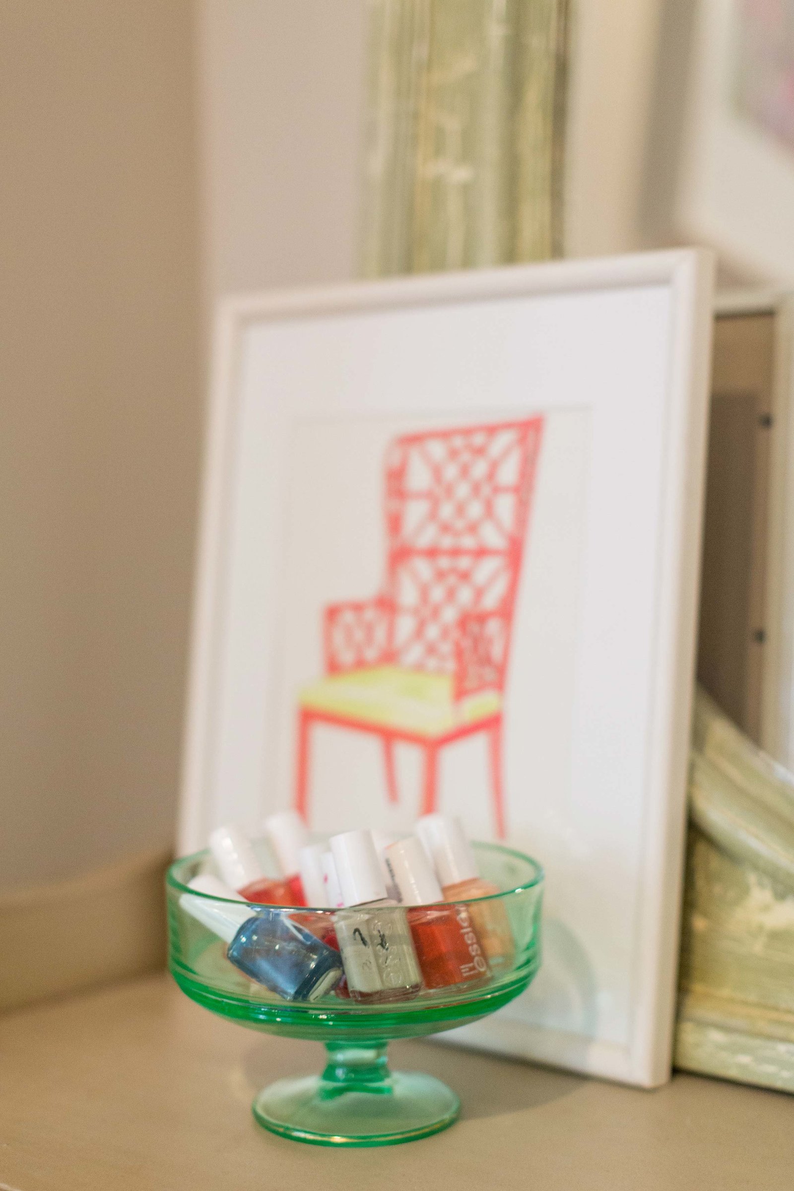 A glass dish with nail polish and a framed print of an orange chair.
