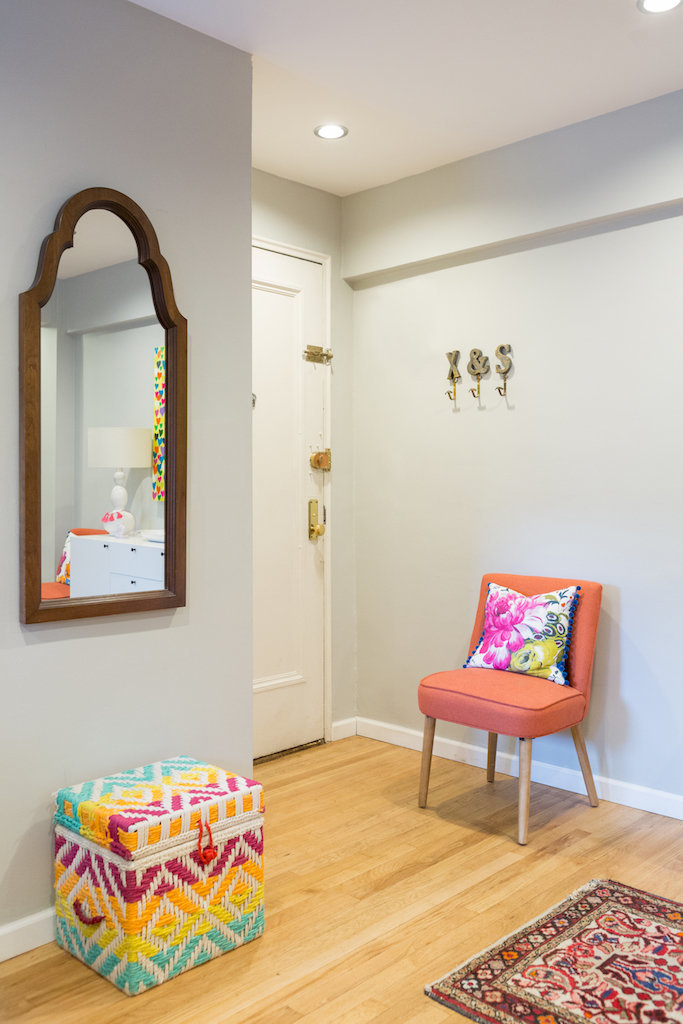 An entry way with an orange chair, colorful basket, hooks, and a mirror.