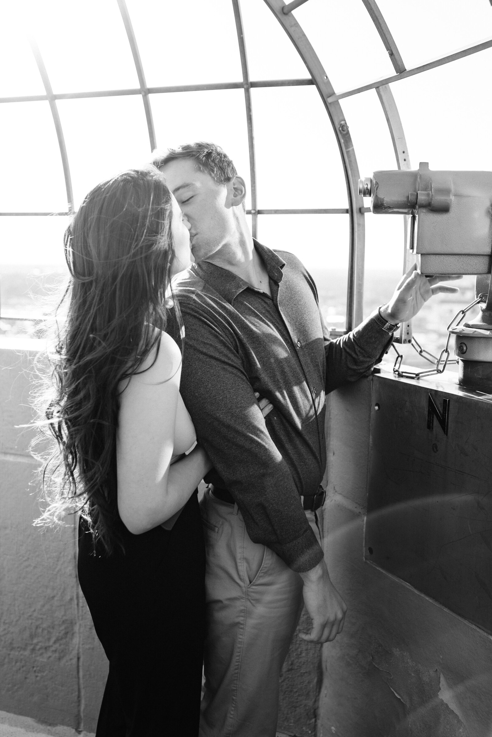 Couple kissing in front of a telescope on the Foshay Tower Observation Deck.