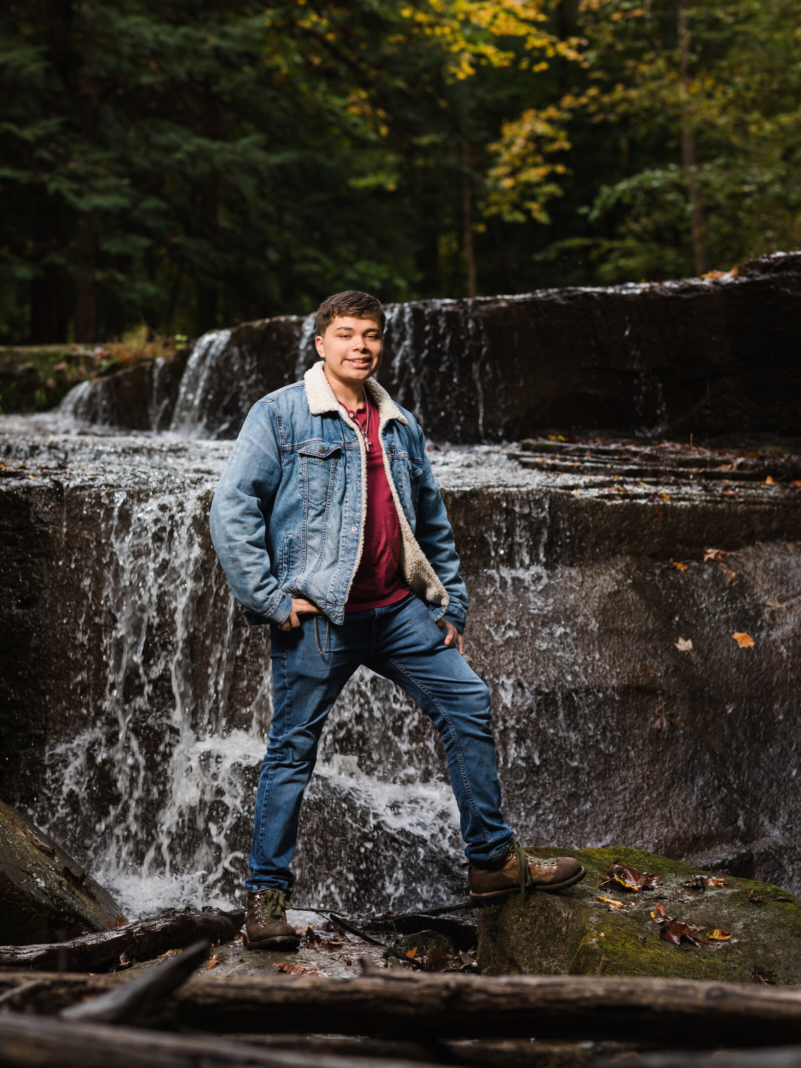 senior boy in jean jacket posing by waterfalls