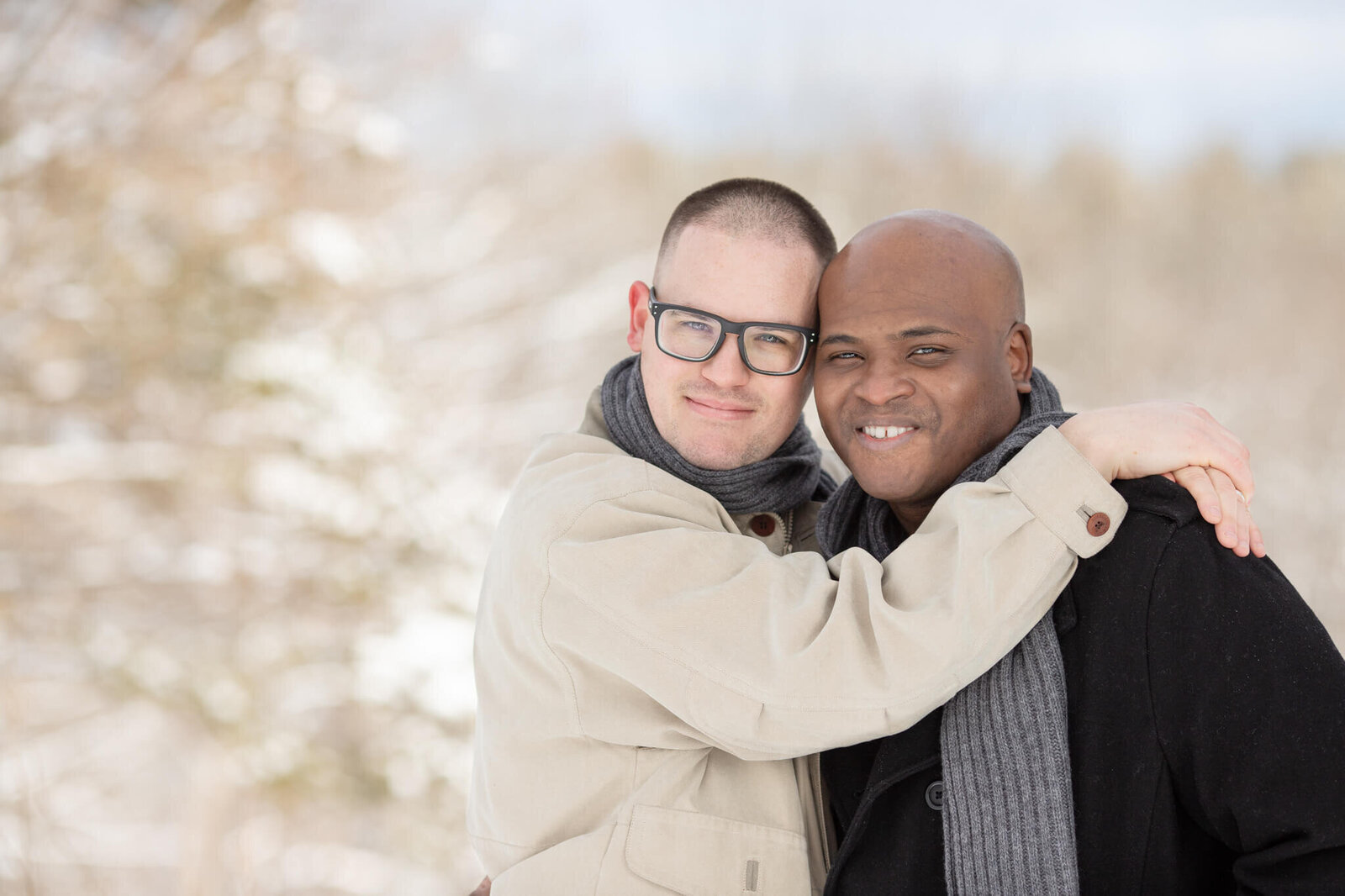 Two males in LGBT relationship hugging facing camera wearing winter coats and scarves