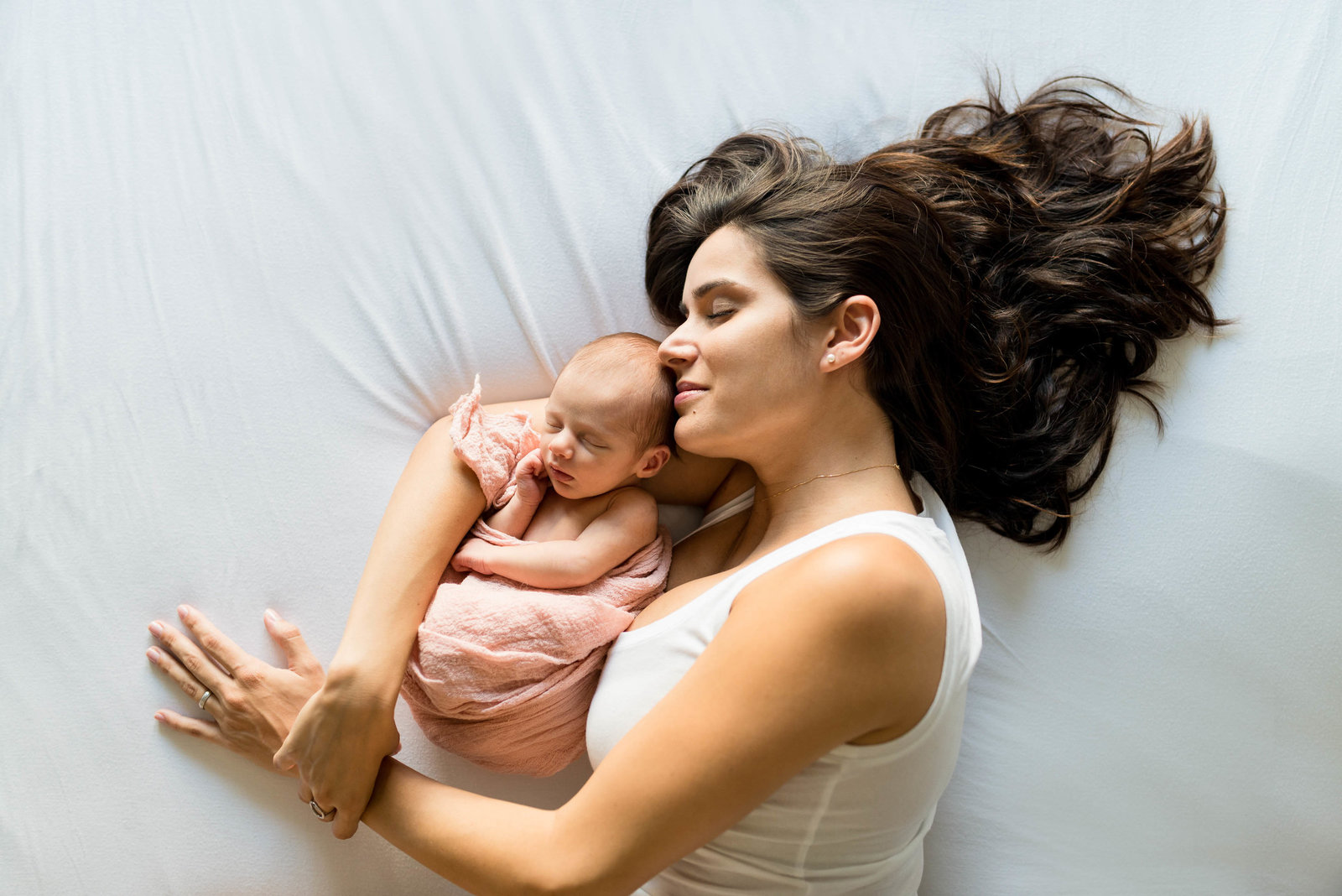 Mom holding newborn lying on bed with hair