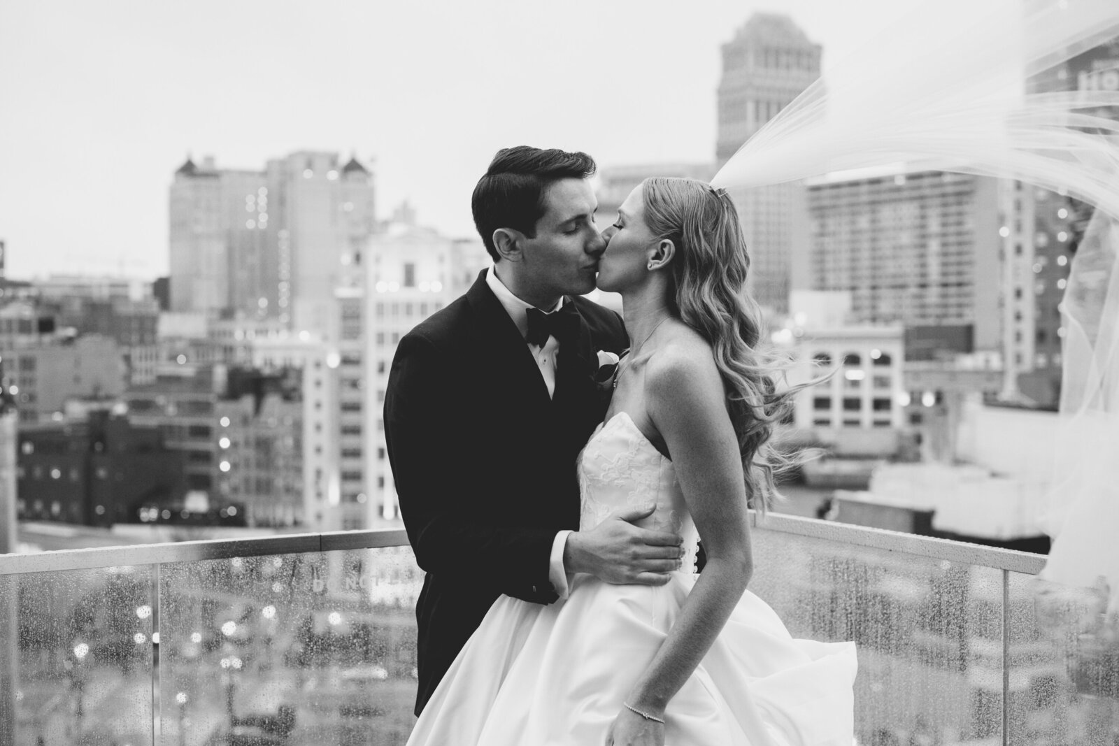 A bride and groom kiss on a rooftop overlooking philadelphia.