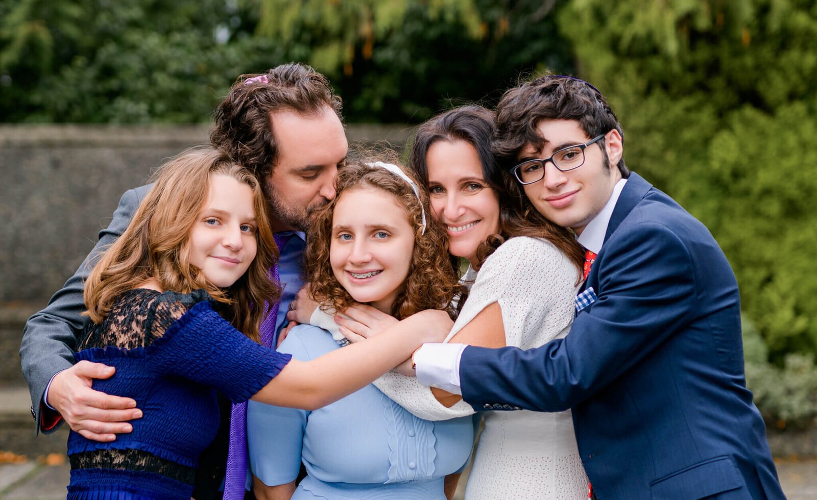 A teen girl is hugged by her parents and big brother and sister in a temple garden