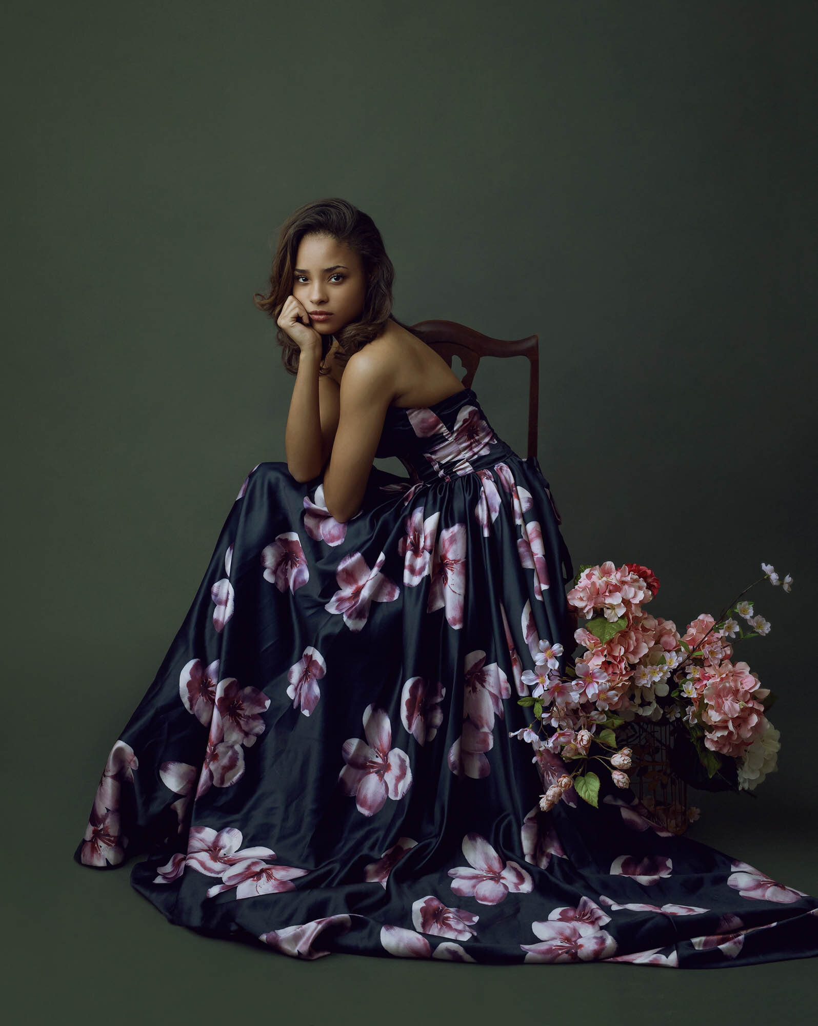 Luxury portrait of a woman in large floral dress, sitting on a chair facing the camera. Houston fine art portraiture.