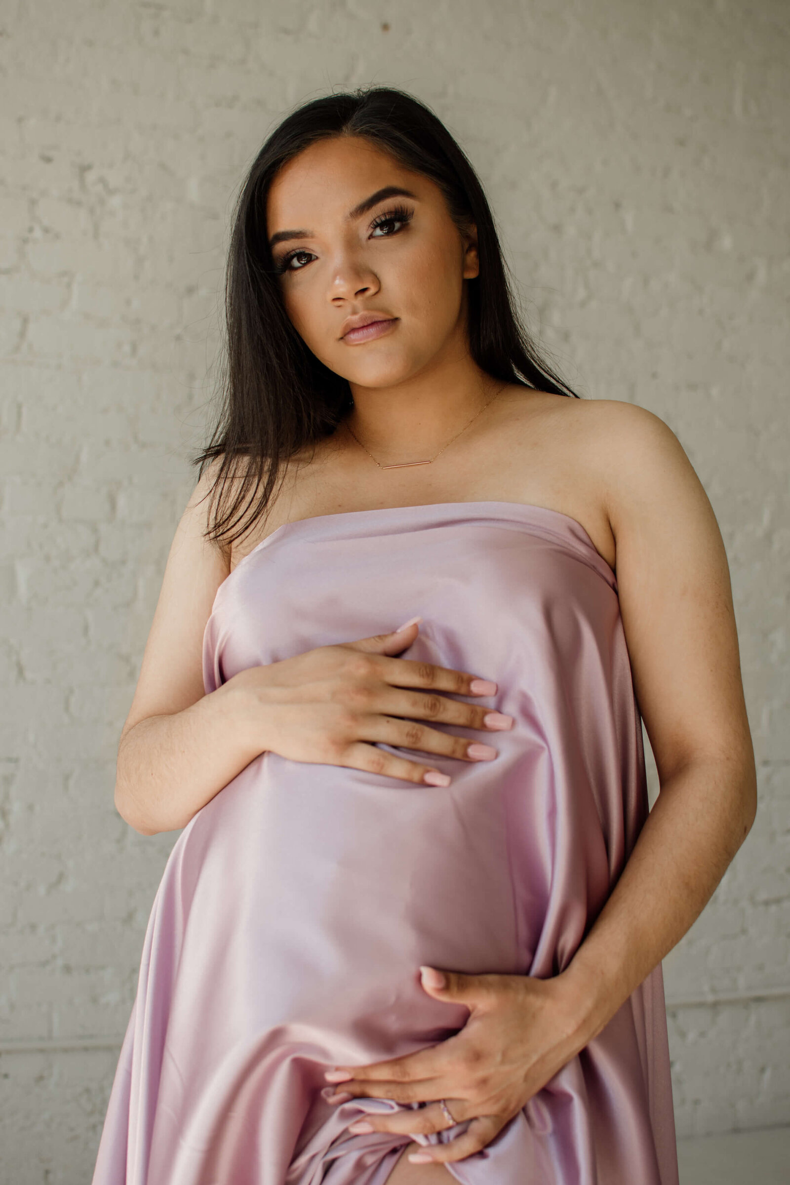 Pregnant woman holding pink satin fabric over belly.