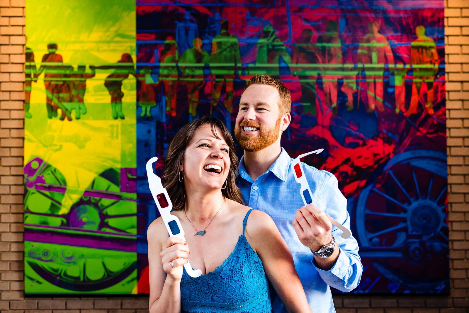 engaged couple in blue outfits poses with 3d glasses in front of a 3d mural in Durham, NC